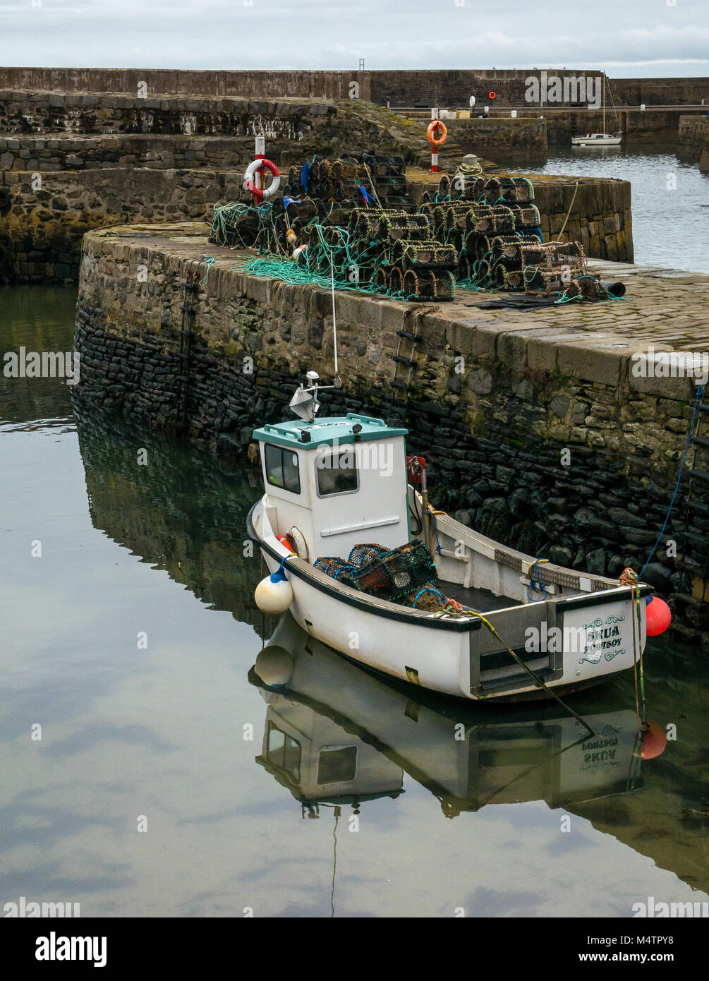 Piccola barca da pesca denominata Skua a bassa marea, porto pittoresco, Dinnet, Aberdeenshire, Scozia, con acqua riflessioni e astice pentole su pier Foto Stock