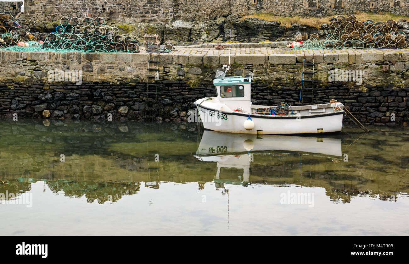 Piccola barca da pesca con la bassa marea, porto pittoresco, Dinnet, Aberdeenshire, Scozia, con acqua riflessioni e astice pentole su pier Foto Stock
