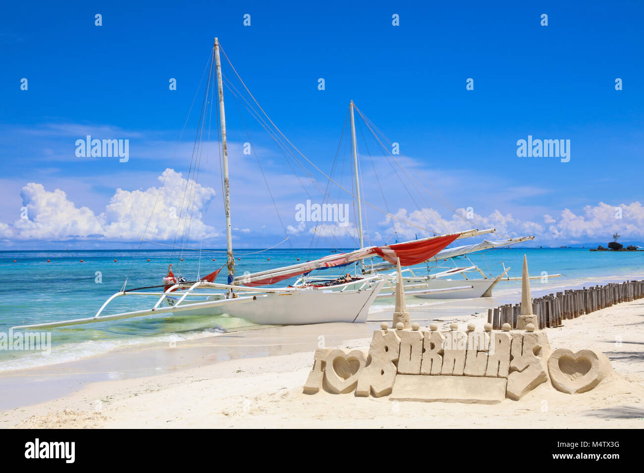 Castello di sabbia in una forma di I LOVE BORACAY e barche di pescatori locali sulla spiaggia bianca, Boracay Island, Filippine. Vacanze tropicali. Foto Stock