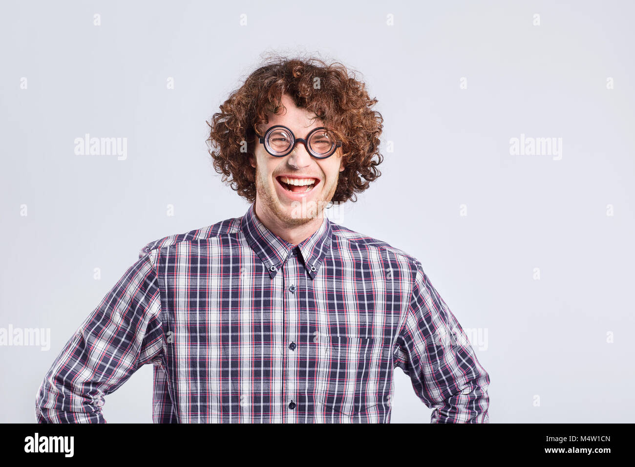 Curly nerd uomo in bicchieri con uno stupido tipo di emozione divertente. Foto Stock