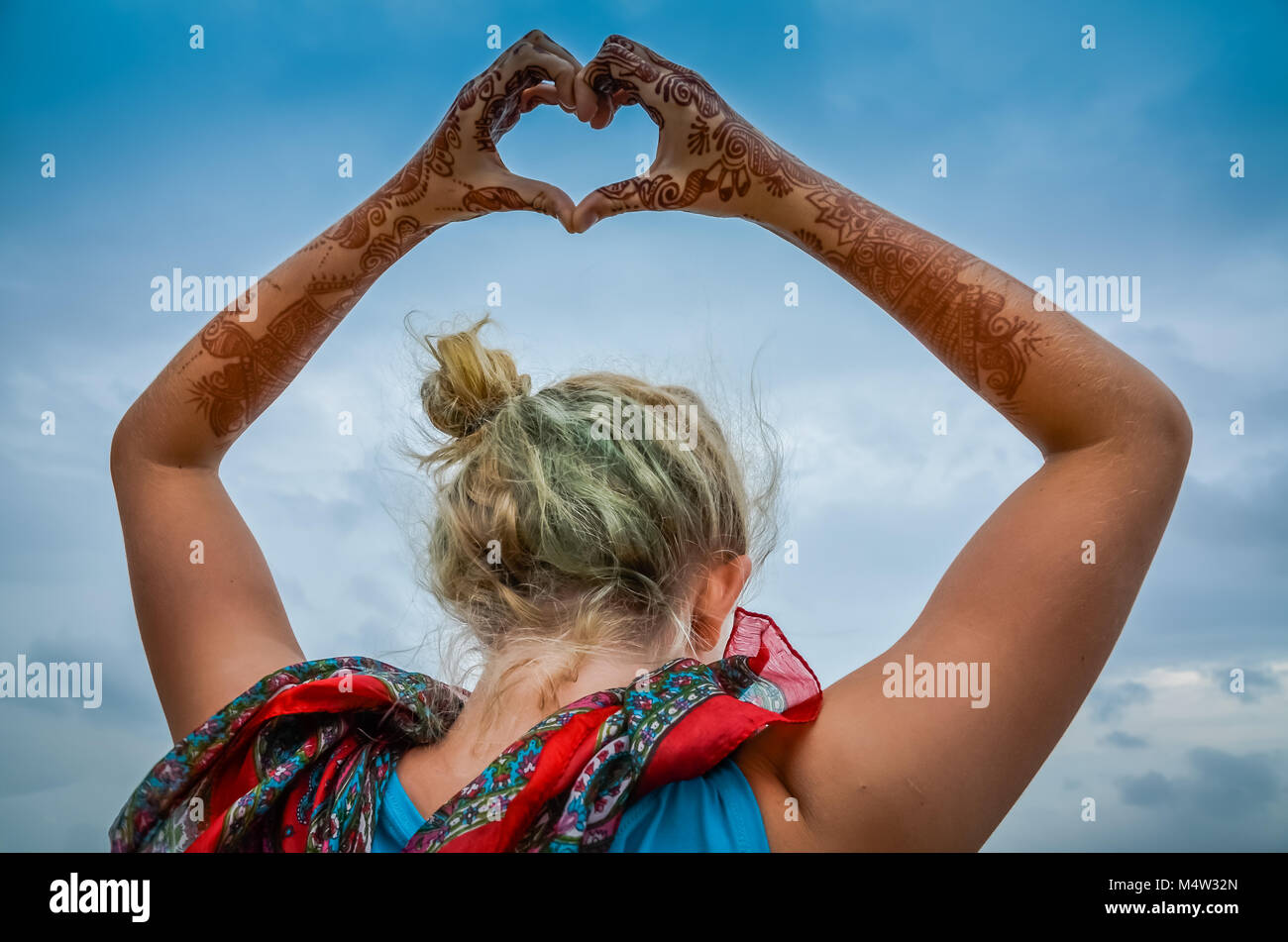 Bella ragazza bionda pone con henna dipinto le mani e le braccia sopra la sua testa a forma di cuore. Foto Stock