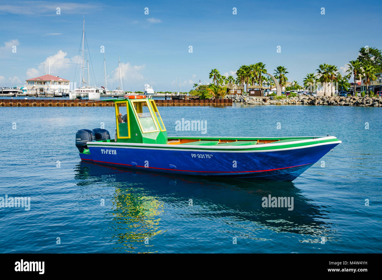 Vivid speedboat--dipinte in colori tropicali di sfumature di verde, blu e giallo--è riflessa sull oceano turchese porto di Gustavia in St. Barths. Foto Stock
