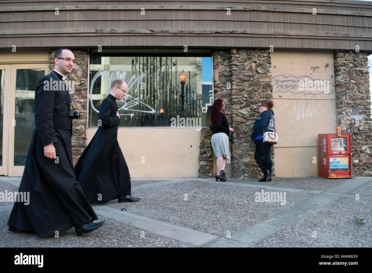 Due donne chat in Sacramento mentre i sacerdoti a piedi giù per la strada. Foto Stock