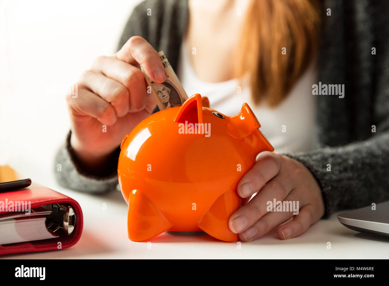 Donna inserendo dollaro in un salvadanaio in casa nel salotto o ufficio Foto Stock