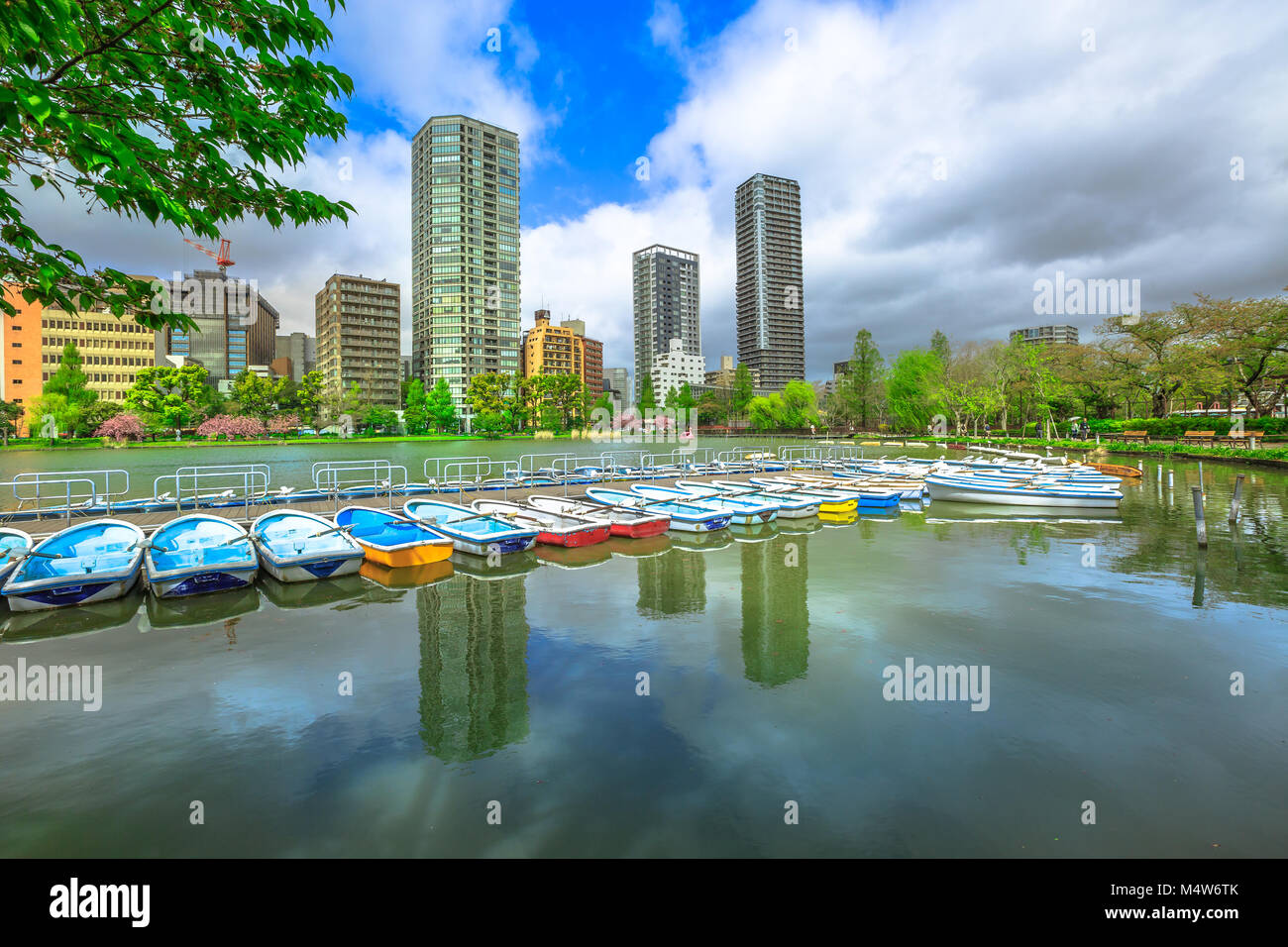 Barche a pedali e grattacieli di Tokyo riflettendo sul laghetto di Shinobazu nel Parco di Ueno, un parco pubblico accanto alla stazione di Ueno nel centro di Tokyo. Il Parco Ueno è considerata la migliore a Tokyo per la fioritura dei ciliegi. Foto Stock