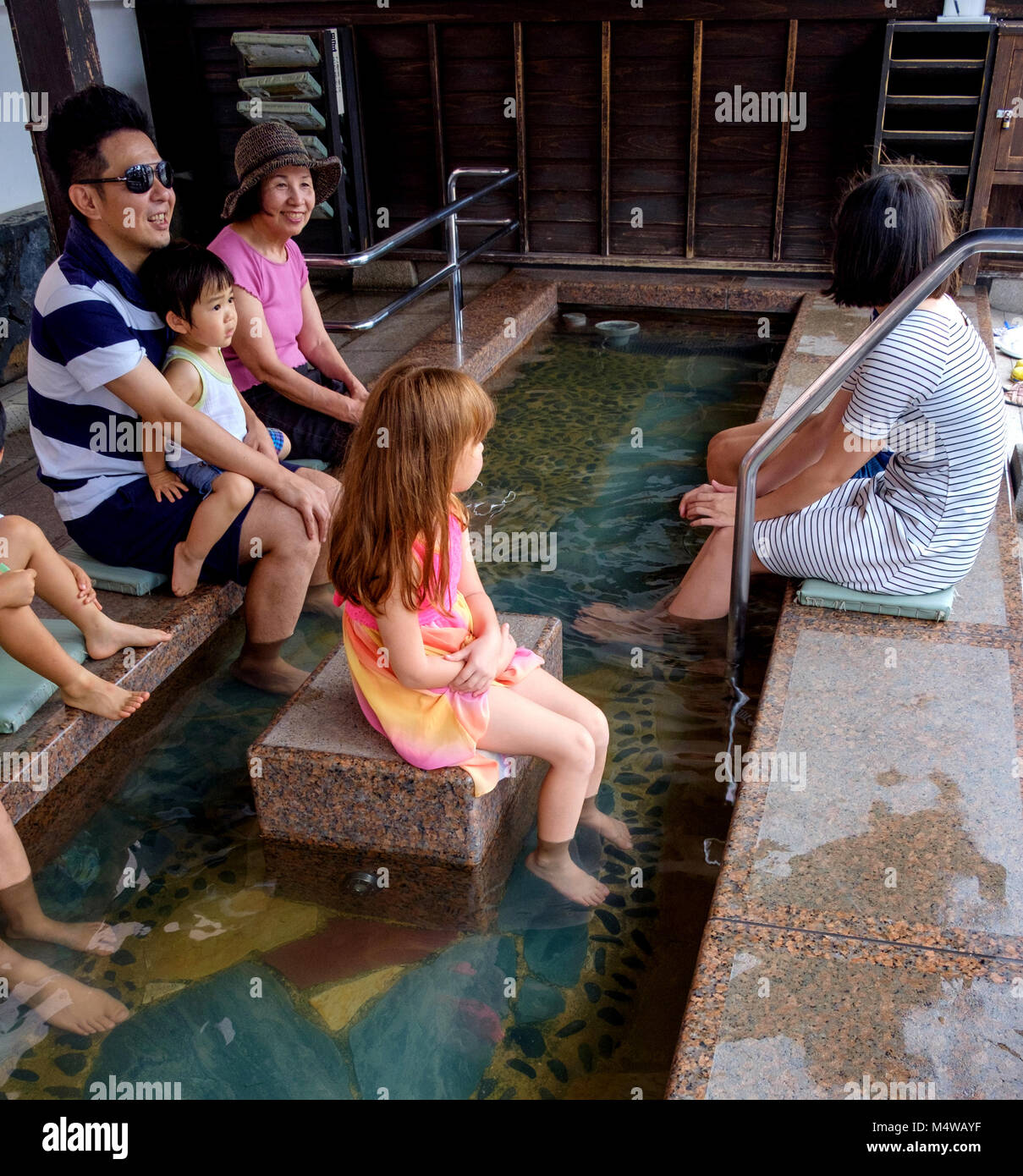 Famiglia giapponesi piedi ammollo in hot springs pediluvio. Piccolo Ragazzo seduto sul padre di giro. Western bambina in centro. Hirado, di Nagasaki, Giappone Foto Stock