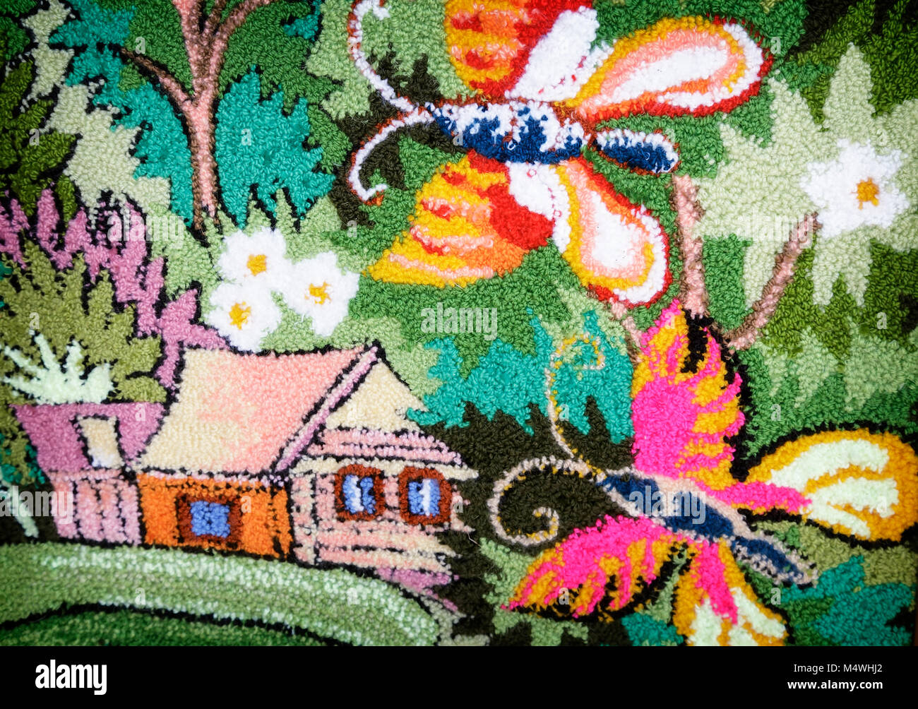Nella parte di vimini della tela si può vedere una casa e una farfalla tra i fiori e foglie verdi. Foto Stock