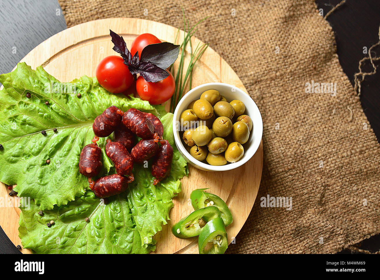 Salsicce di caccia su una tavola di legno con lattuga, basilico, pomodori ciliegini, paprika e olive. Foto Stock