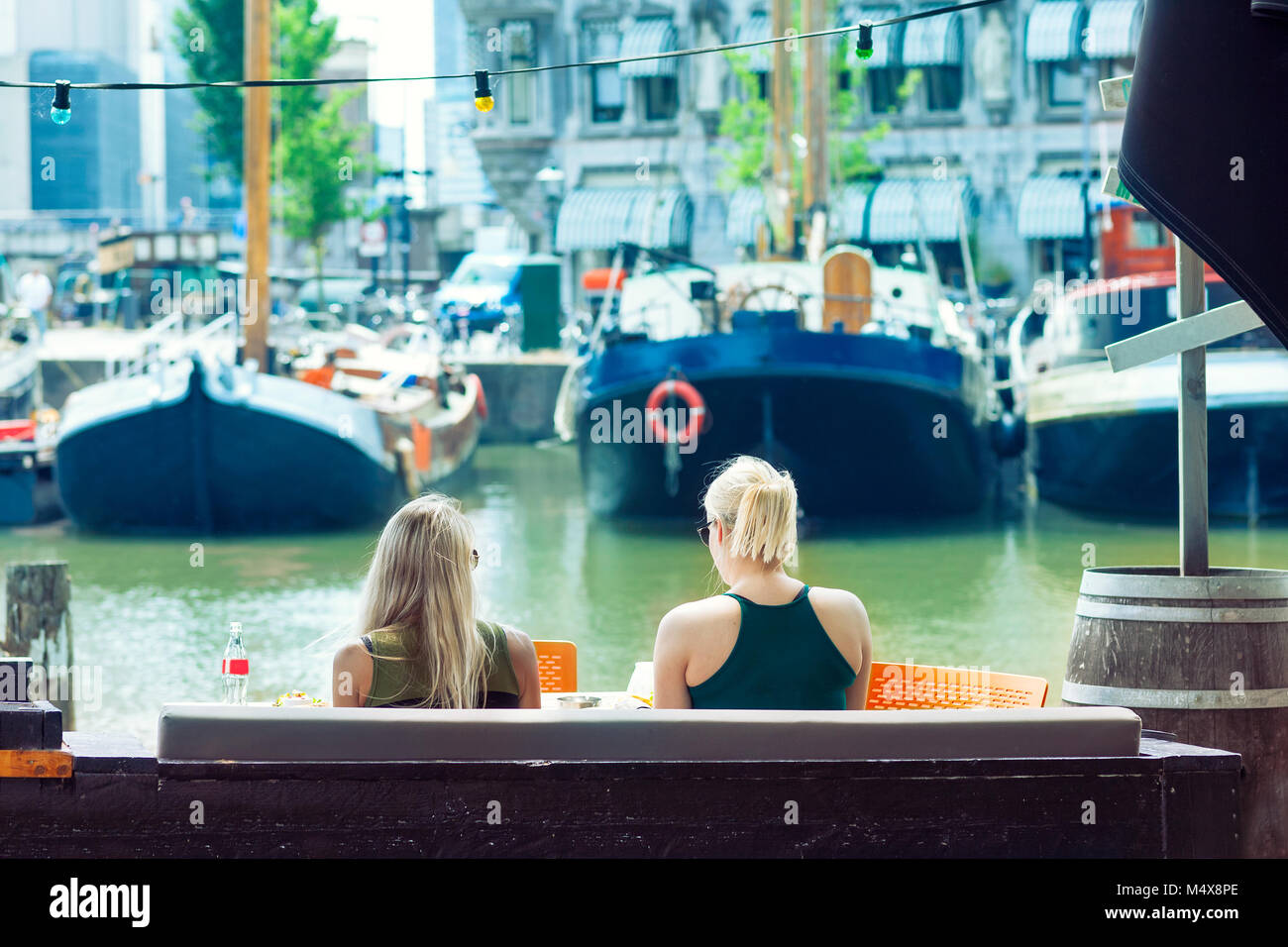 Due giovani donne bionda di bere una bevanda fredda, il porto di Rotterdam in background, Paesi Bassi Foto Stock