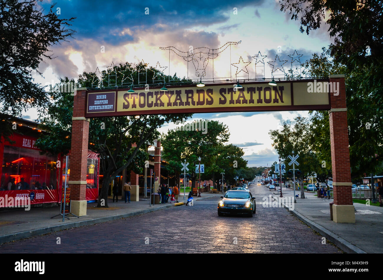 Fort Worth, Texas. Auto passando sotto il cartello di ingresso al centro storico Fort Worth Stockyards illuminata di sera presto. Foto Stock