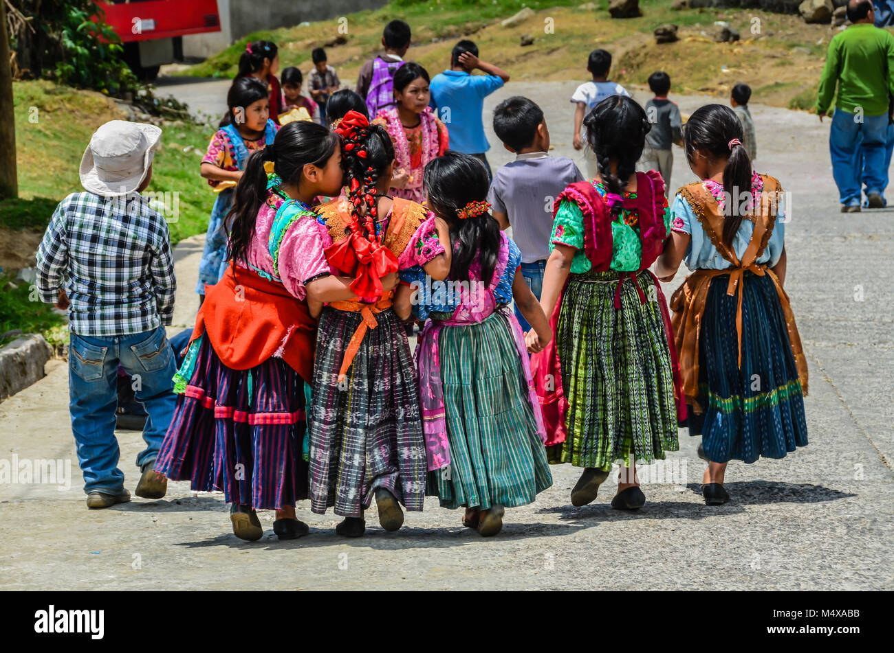 Gruppo di Guatemala i bambini a scuola a piedi sulla strada, tenendo le mani, quando una bambina sussurra in casa di un amico orecchio. Foto Stock