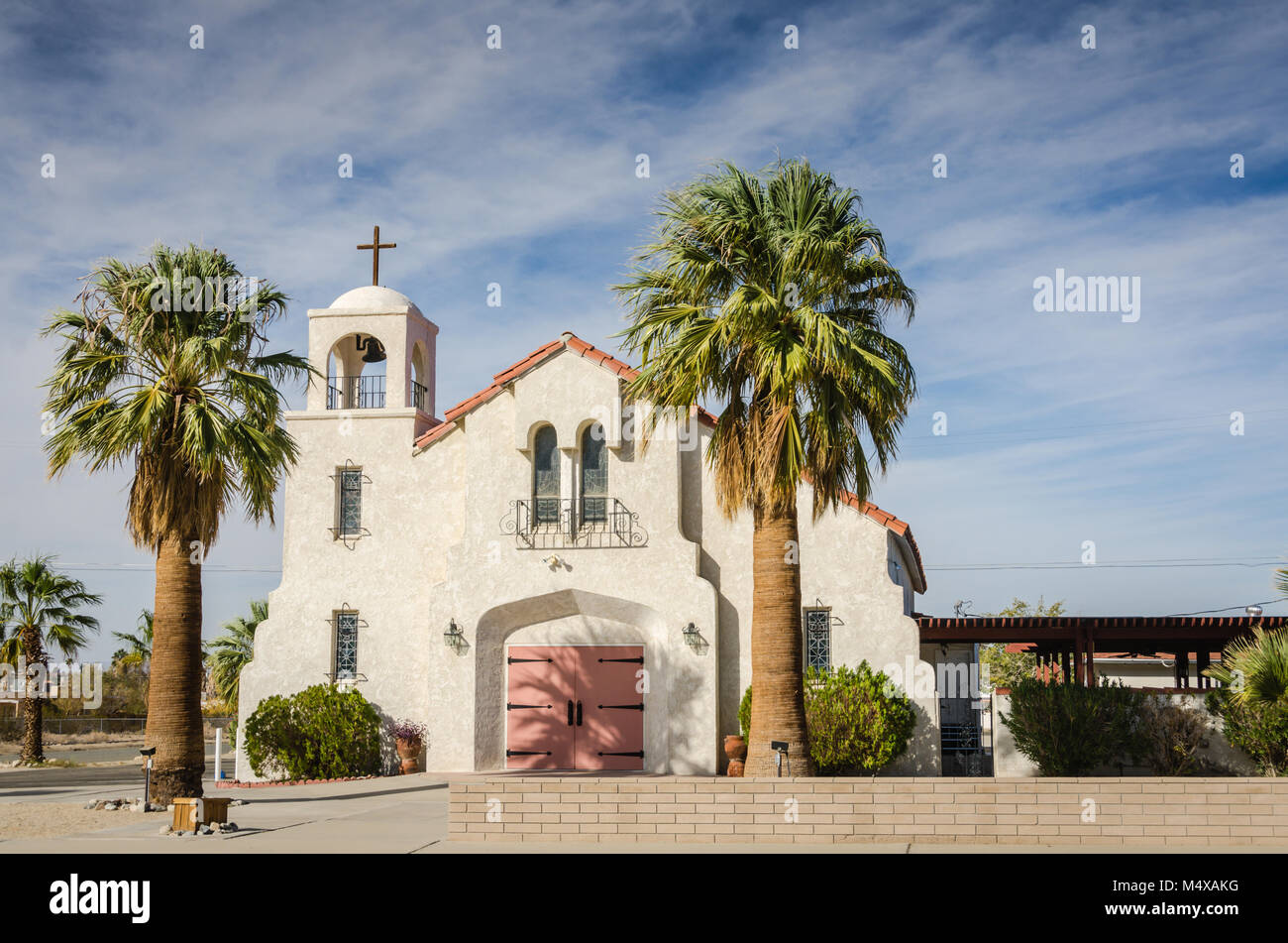 Rosa e Bianco santissimo sacramento la Chiesa e la scuola incorniciato da data palme vicino a Joshua Tree National Park e il Mojave Desert. Foto Stock