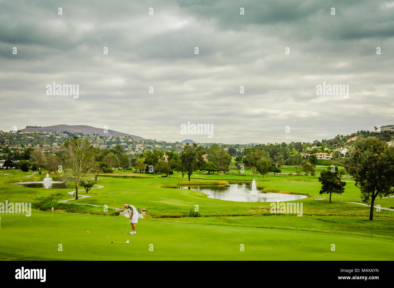 Un golfista mette sul verde del campo da golf nonostante nuvole grigie e pioggia imminente. Foto Stock