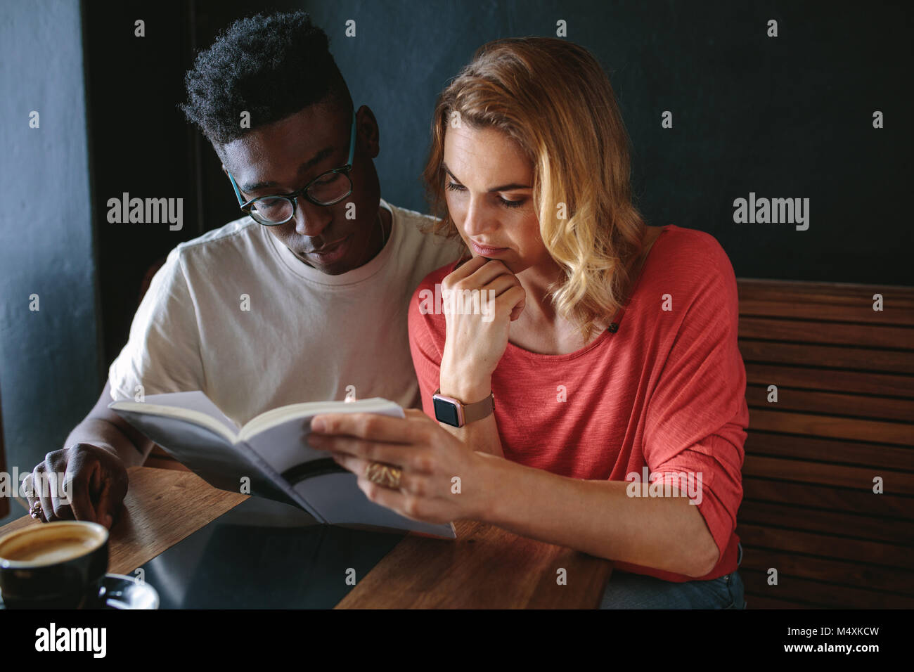 L uomo e la donna seduta al tavolo da caffè la lettura di un libro insieme. Matura in un coffee shop la lettura di un libro con una tazza di caffè sul tavolo. Foto Stock