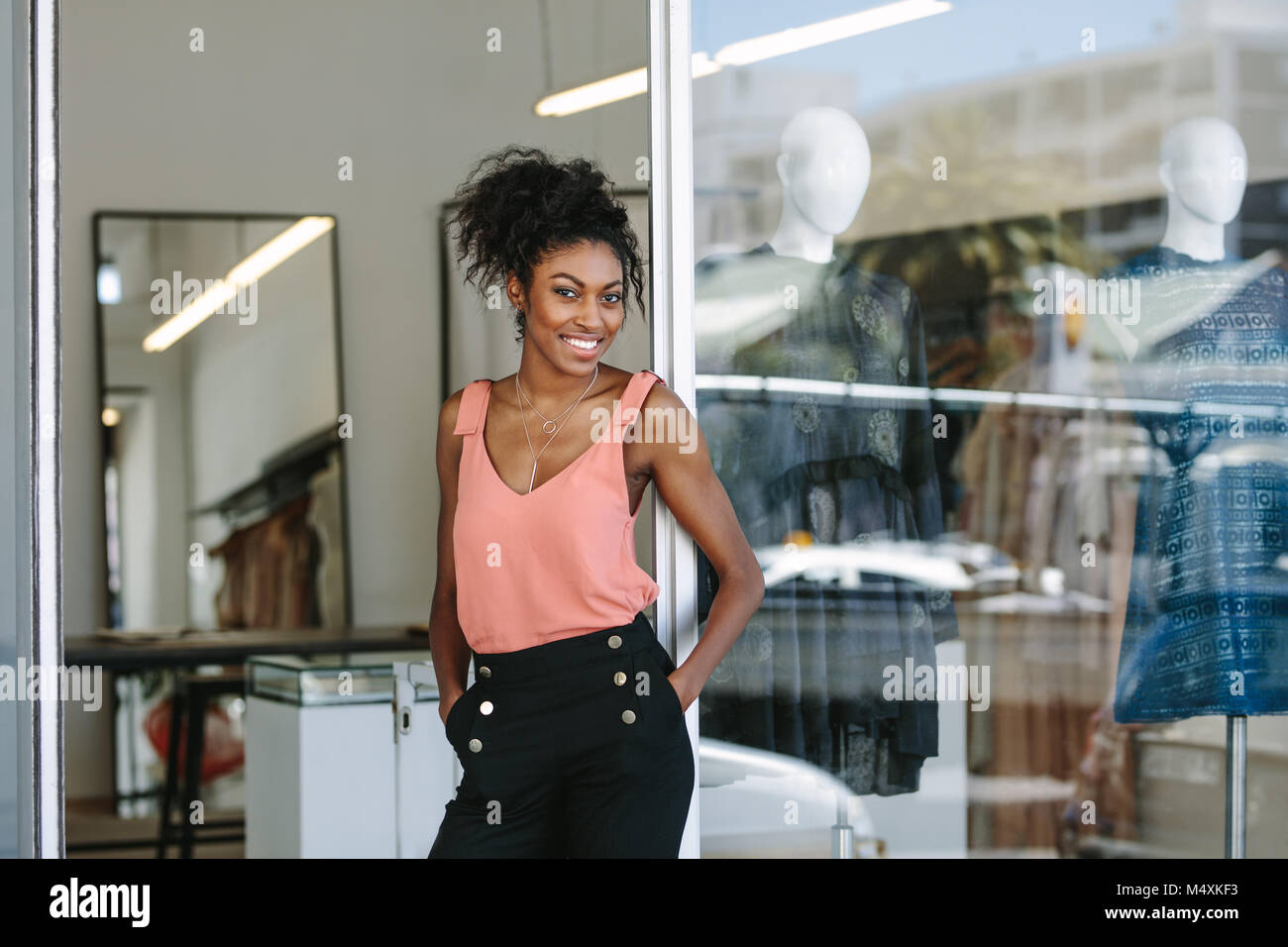 Abito sorridente designer nel suo negozio di stoffa con abiti firmati sul display. Imprenditrice donna in piedi all'ingresso del suo studio di moda. Foto Stock