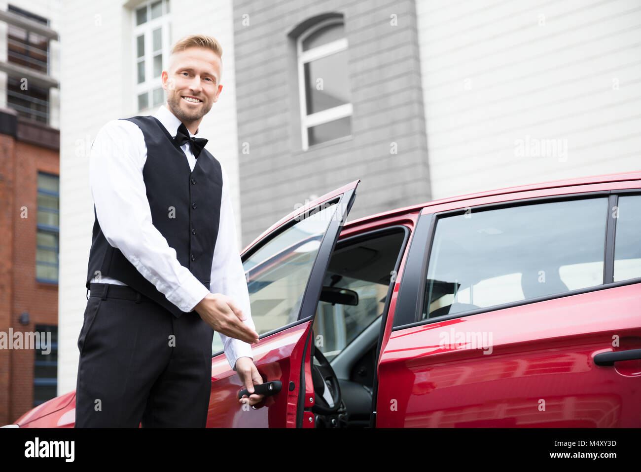 Ritratto di un bel giovane maschio apertura Servizio di presa e consegna auto rossa porta Foto Stock