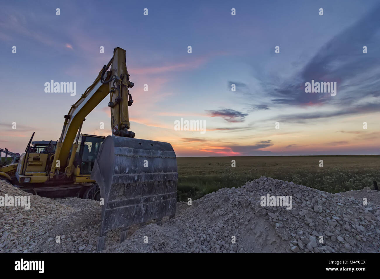 Un arresto escavatore giallo a un incredibilmente bellissimo tramonto Foto Stock