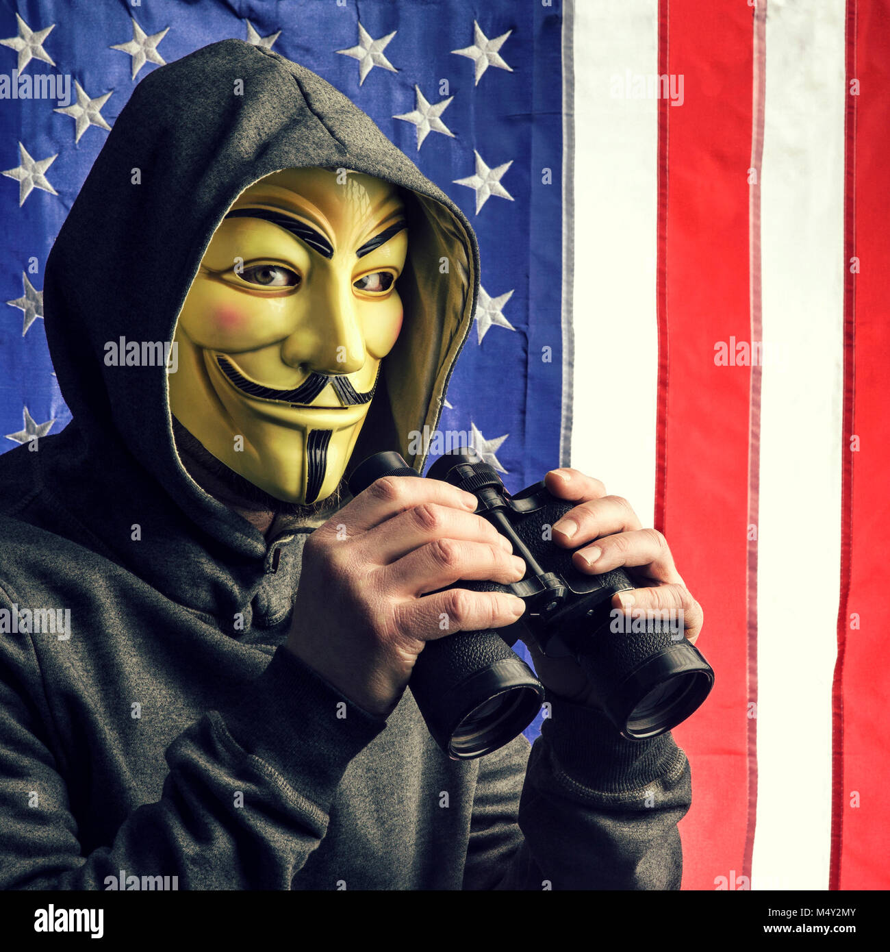 Milano,Italia, Febbraio 2018: Hacker tenendo il binocolo indossare maschera anonimi con american vecchia gloria bandiera in background.foto editoriale. Foto Stock