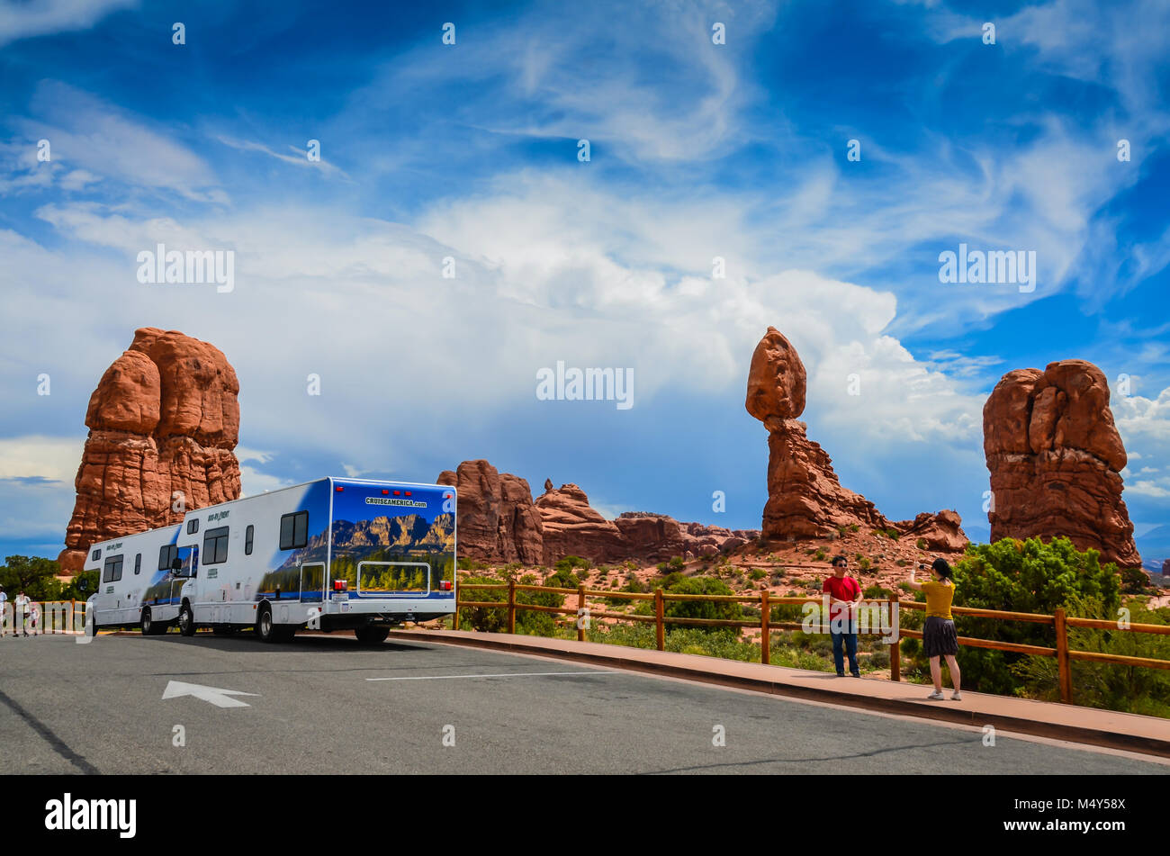 Turisti asiatici scattare fotografie di fronte equilibrato di Rock, mentre due RVs rimangono parcheggiate dalla meraviglia naturale. Parco nazionale Great Basin, Moab, UT Foto Stock