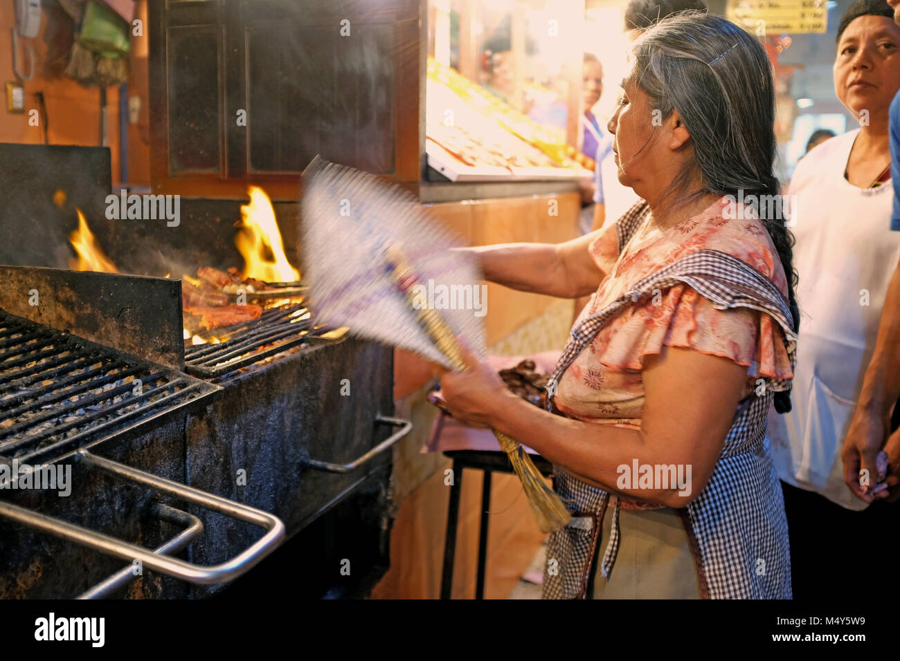 Donna ventole fiamme durante la cottura la famosa carne Oaxacan su open-grill all'interno del Mercado de la comida a Oaxaca, Messico. Foto Stock