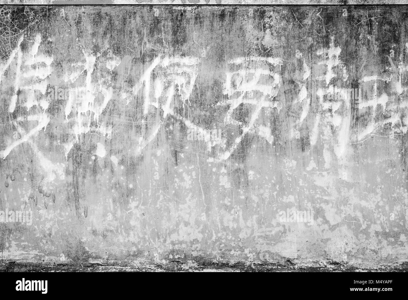 A spiovente e di età compresa tra la parete di calcestruzzo sfondo texture con alcuni sbiadito scrittura cinese in bianco e nero. Foto Stock