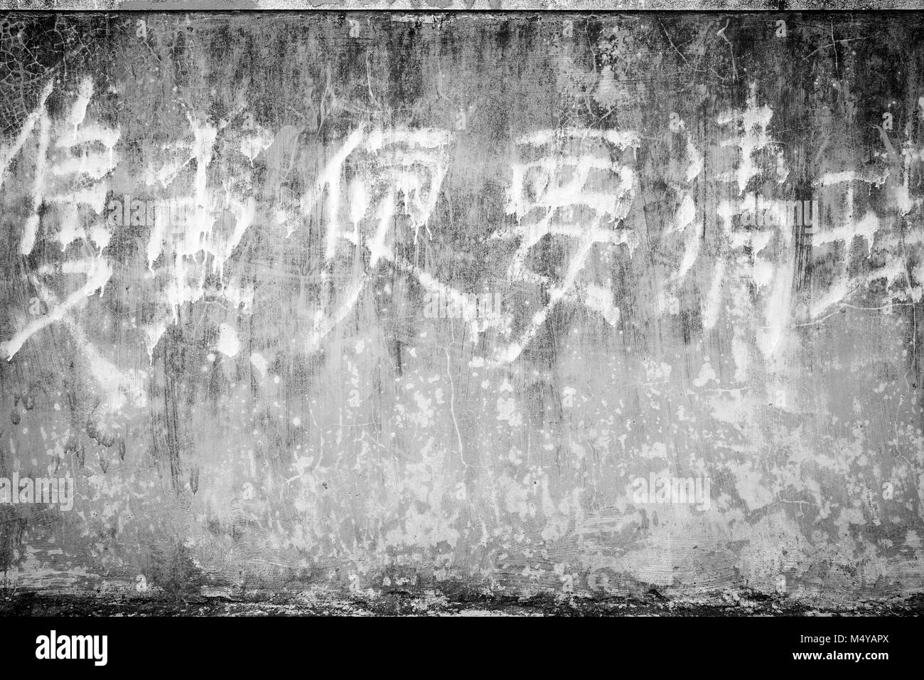 A spiovente e di età compresa tra la parete di calcestruzzo sfondo texture con alcuni sbiadito scrittura cinese in bianco e nero con la vignettatura. Foto Stock