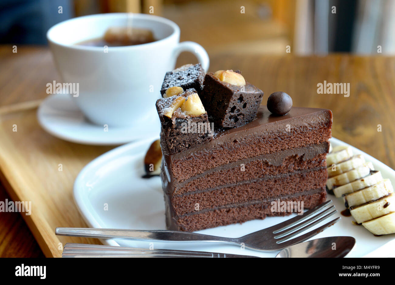Torta al cioccolato sul piatto al tavolo di coffeeshop foto in interni e alcuni apparecchi di illuminazione per esterni. Foto Stock