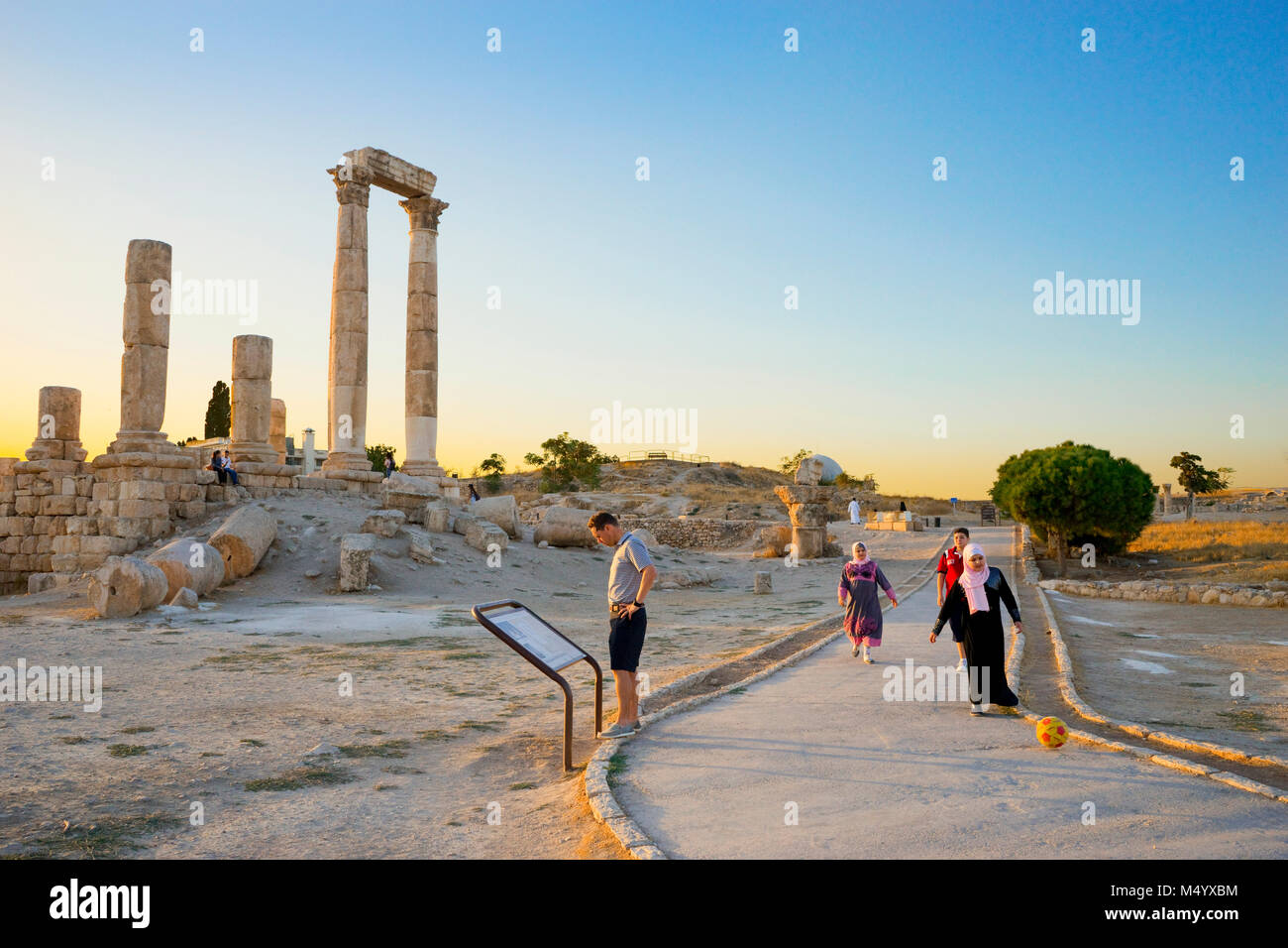 L'uomo per la lettura di informazioni segno e i bambini giocando con il pallone da calcio al Tempio di Ercole nella cittadella di Amman, Amman, Giordania Foto Stock