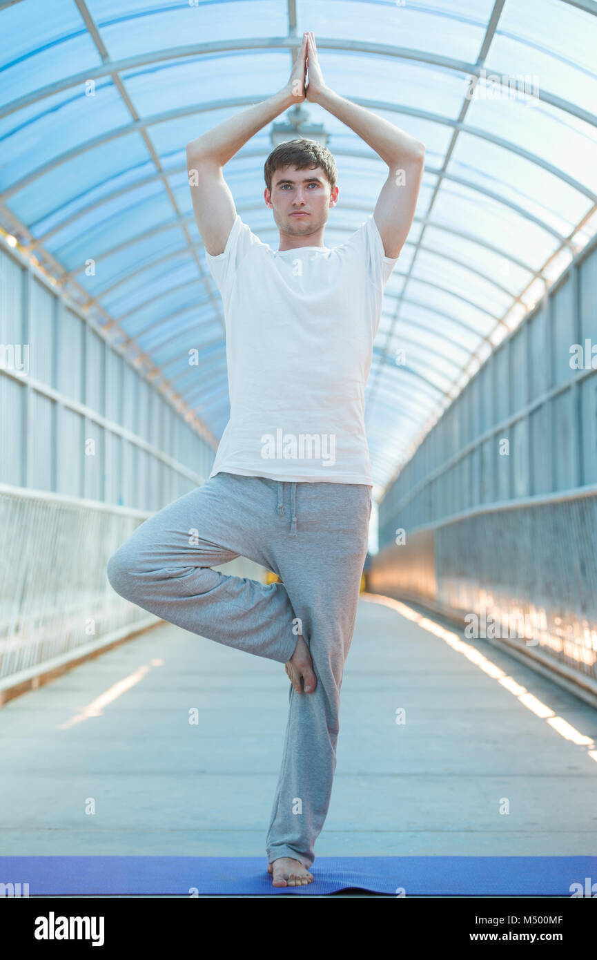 Montare il giovane uomo le pratiche yoga sul ponte Foto Stock