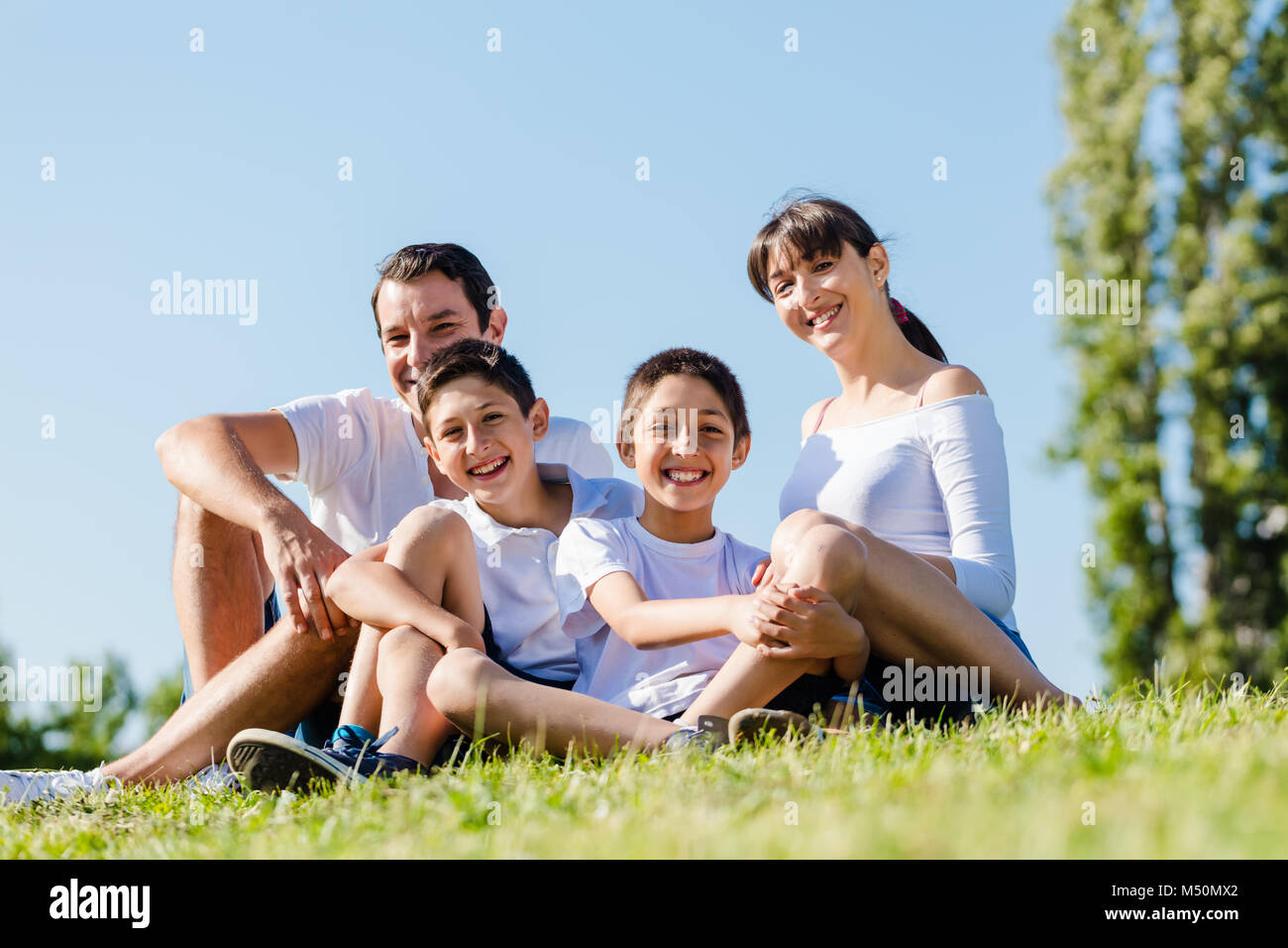 Famiglia vestita di bianco nel parco in estate seduta in Prato Foto Stock