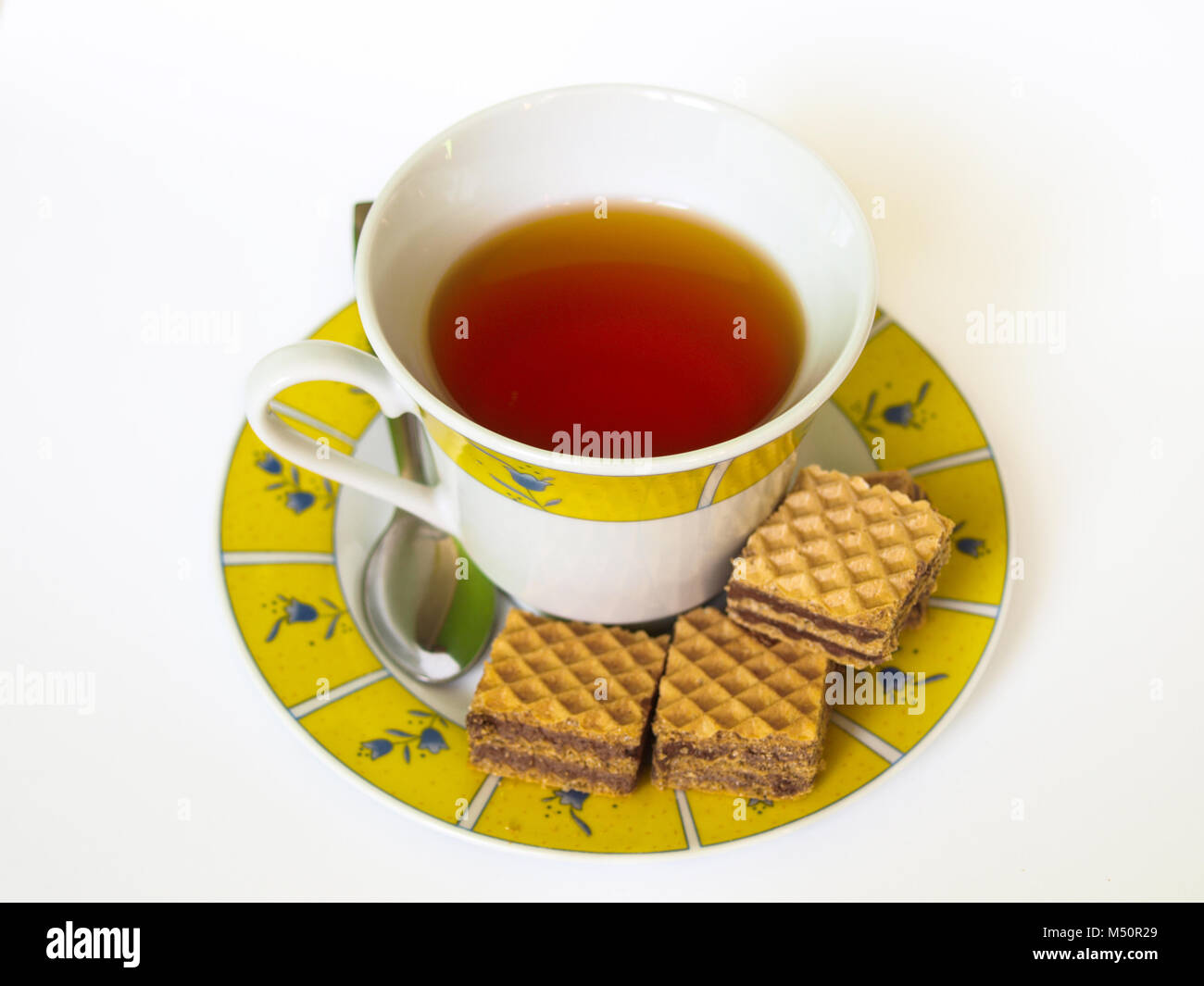 Tazza di tè con wafer al cioccolato, metallo cucchiaino, motivi floreali Piastra piccola, bianco su sfondo isolato. Foto Stock