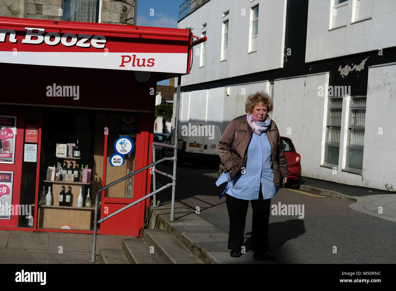 Una donna che cammina davanti a un off-licenza in Newquay, Cornwall Foto Stock