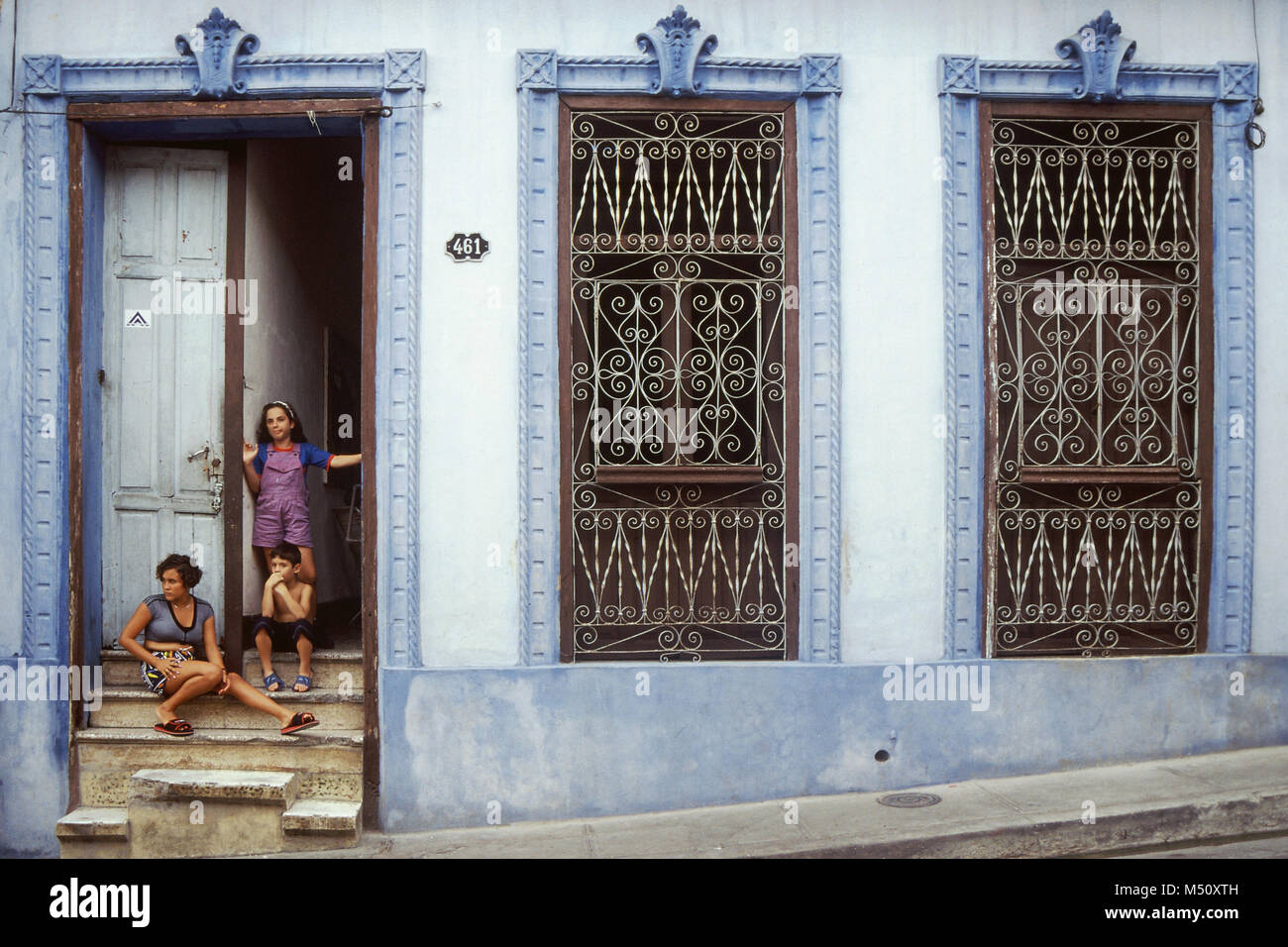 Vista frontale della madre locali e posti a sedere per bambini sui gradini della loro casa nella piccola città coloniale di Trinidad, Cuba Foto Stock