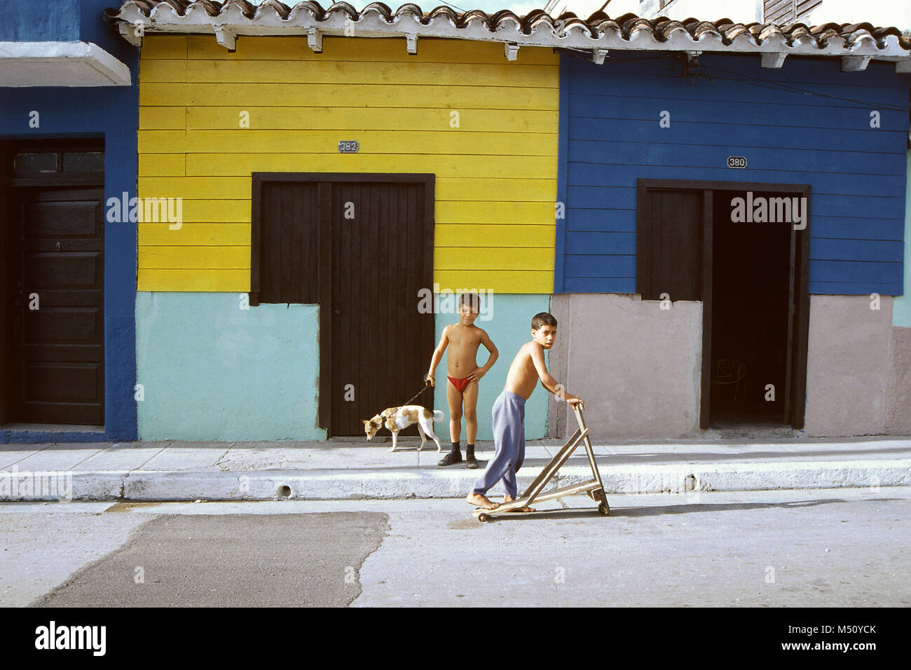 Due ragazzi, uno con un cane e uno con uno scooter in un quartiere povero, Trinidad, Cuba Foto Stock