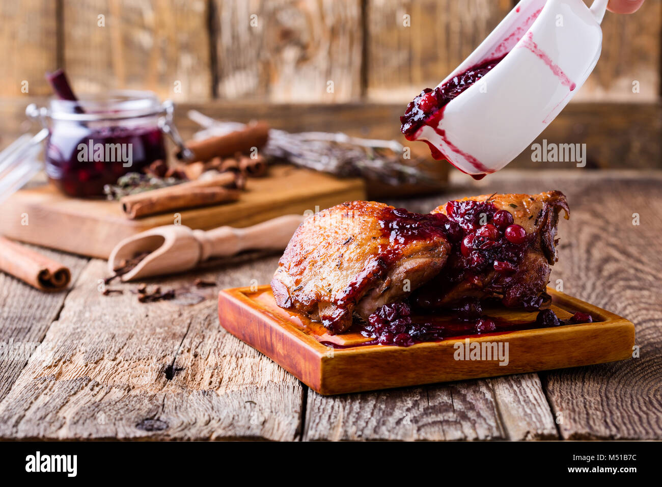 Pollo arrosto gambe sul bordo di taglio servito con salsa di mirtilli su tavola in legno rustico Foto Stock