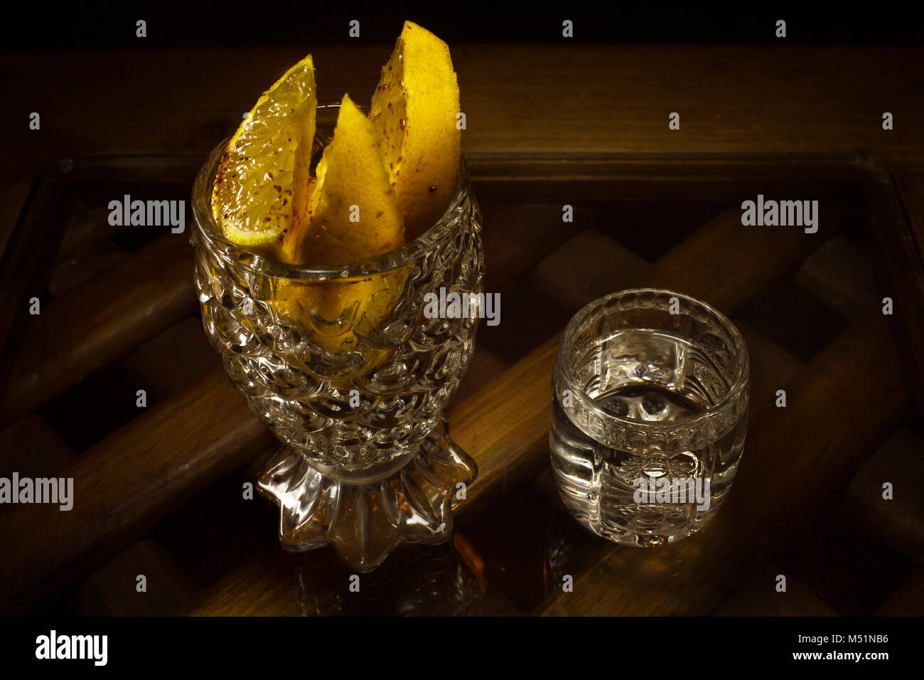 Mezcal messicano in un bicchiere accanto alla tazza di cristallo con fette di arance su un marrone tavolo in legno Foto Stock