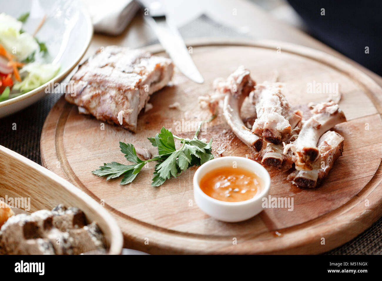 Le costole. l uomo nel ristorante con un coltello taglia grigliata di costolette di maiale. Servire su una tavola di legno. Foto Stock