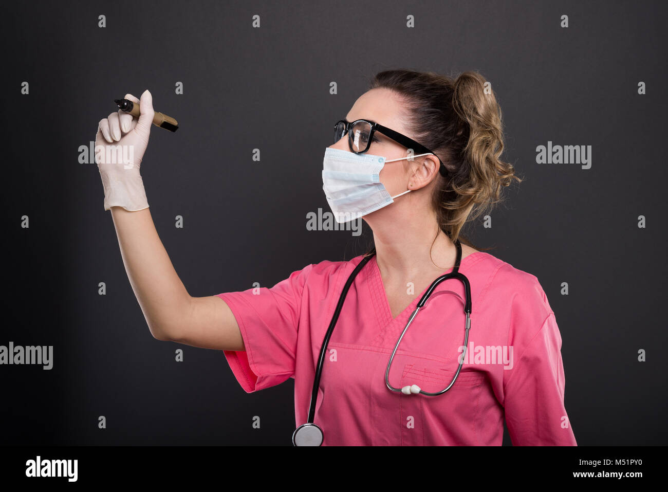 Ritratto di signora attraente medico indossando maschera la scrittura con un pennarello su sfondo nero Foto Stock