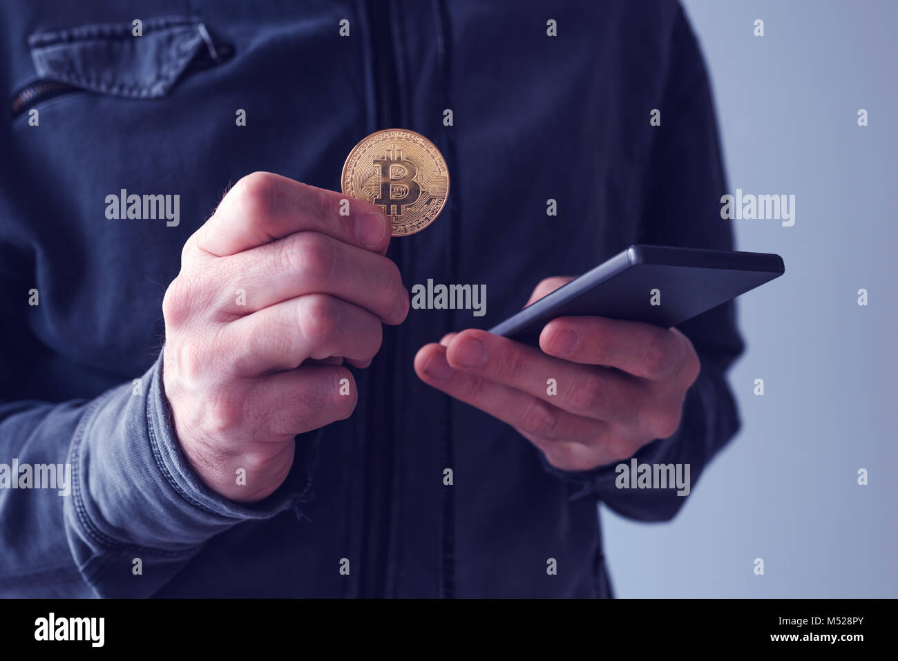 Uomo con bitcoin e il telefono cellulare, la stretta di mano con BTC cryptocurrency moneta e lo smartphone Foto Stock