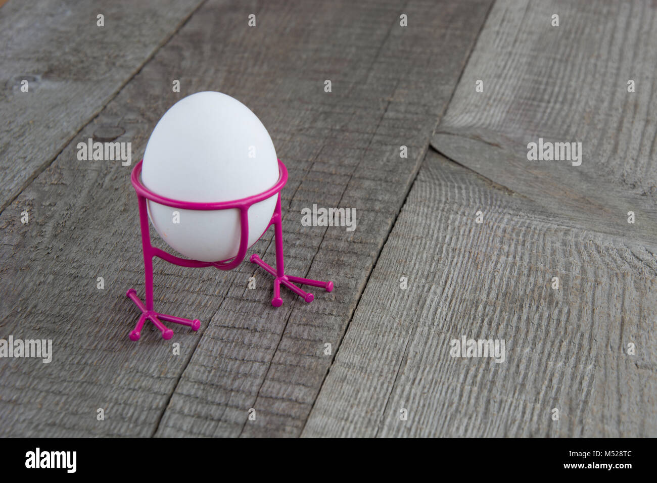 Uovo bianco in rosa divertente stare con le zampe su un sfondo di legno Foto Stock