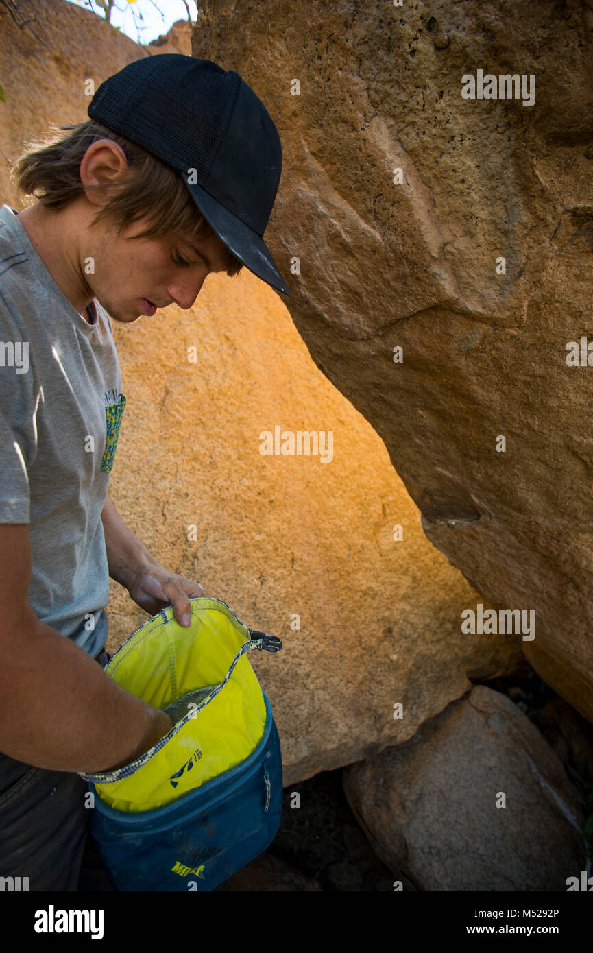 Giovane uomo che coprono le mani in Chalk prima di salire di massi, Brandberg, Damaraland, Namibia Foto Stock