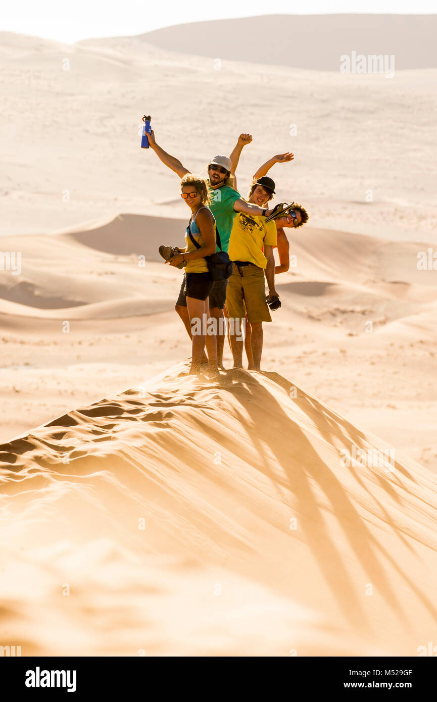 Gruppo di amici in piedi nel deserto del Namib Sorridendo e agitando mentre guardano la telecamera, Namibia Foto Stock