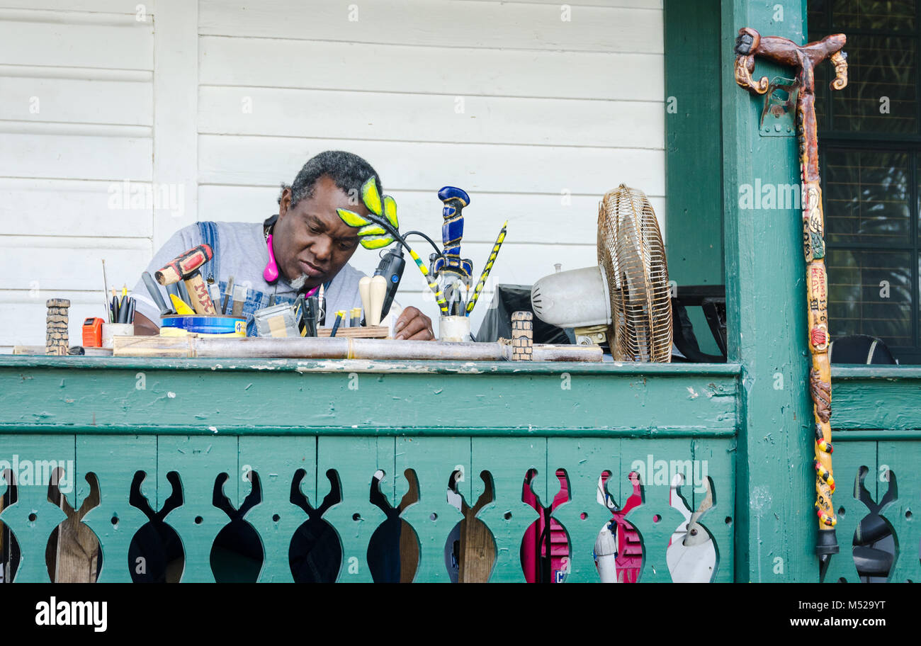 Un uomo si siede a un Key West, FL balcone in legno di incisione da un intricatamente intagliati e dipinti di canna di legno che egli ha fatto. Foto Stock