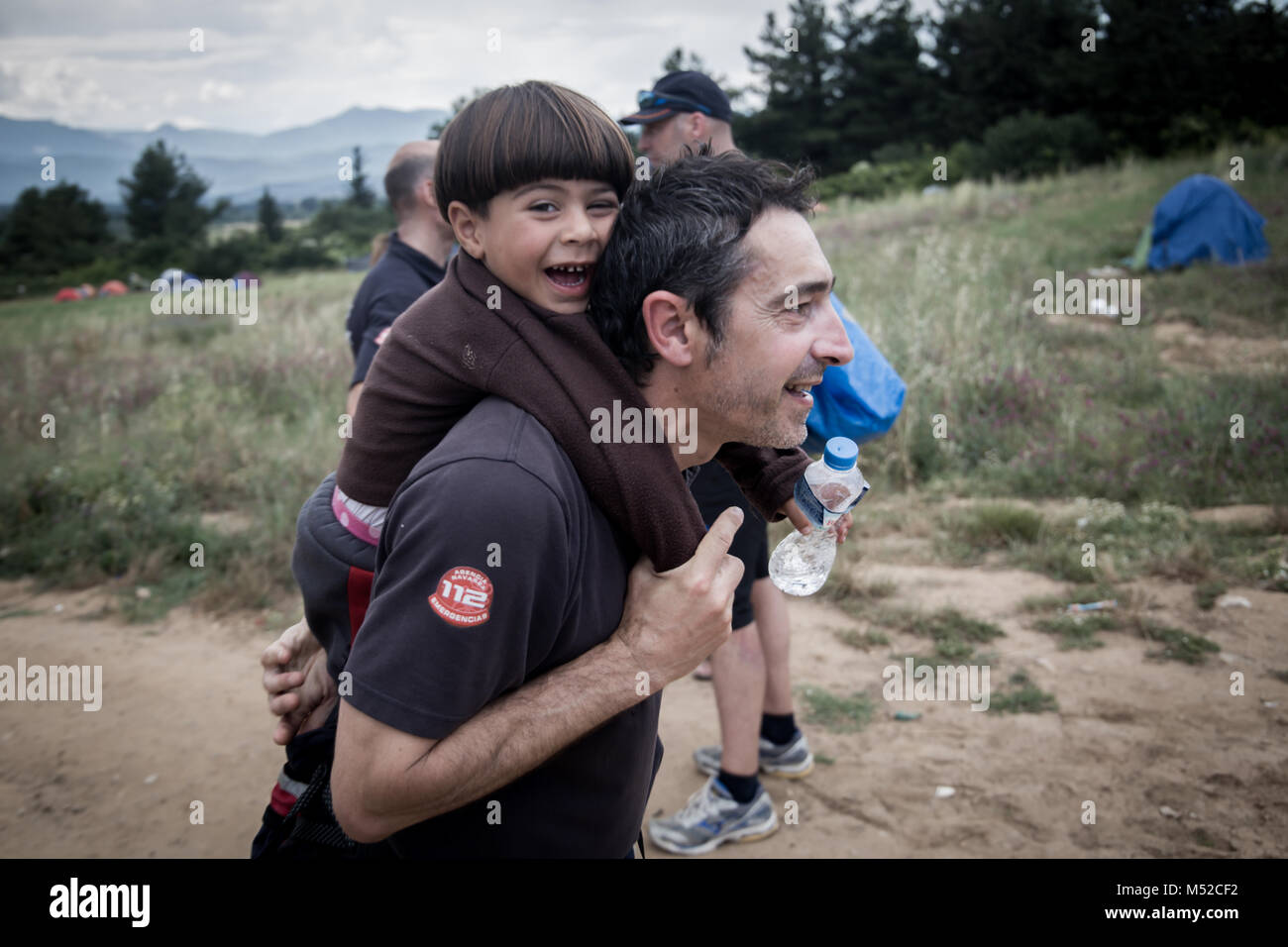 Un volontario spagnolo vigile del fuoco che porta un ragazzo siriano a Idomeni Refugee Camp in Grecia settentrionale. Foto Stock