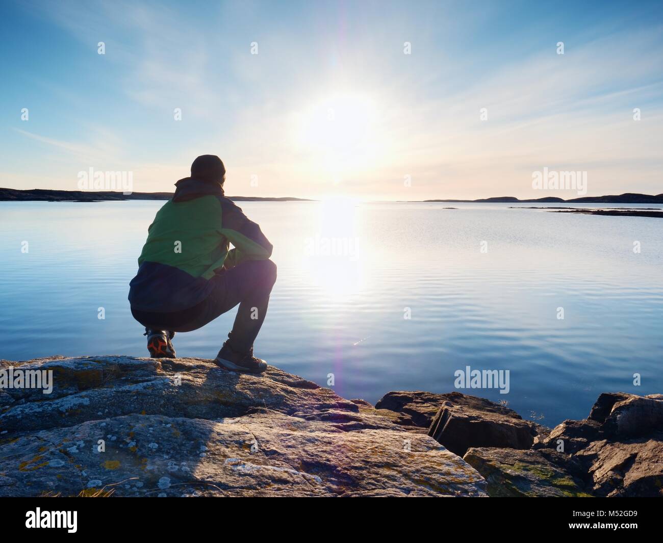 Uomo solitario escursionista si siede da solo sulla costa rocciosa e godersi il tramonto. Vista sulla scogliera rocciosa di oceano libero Foto Stock