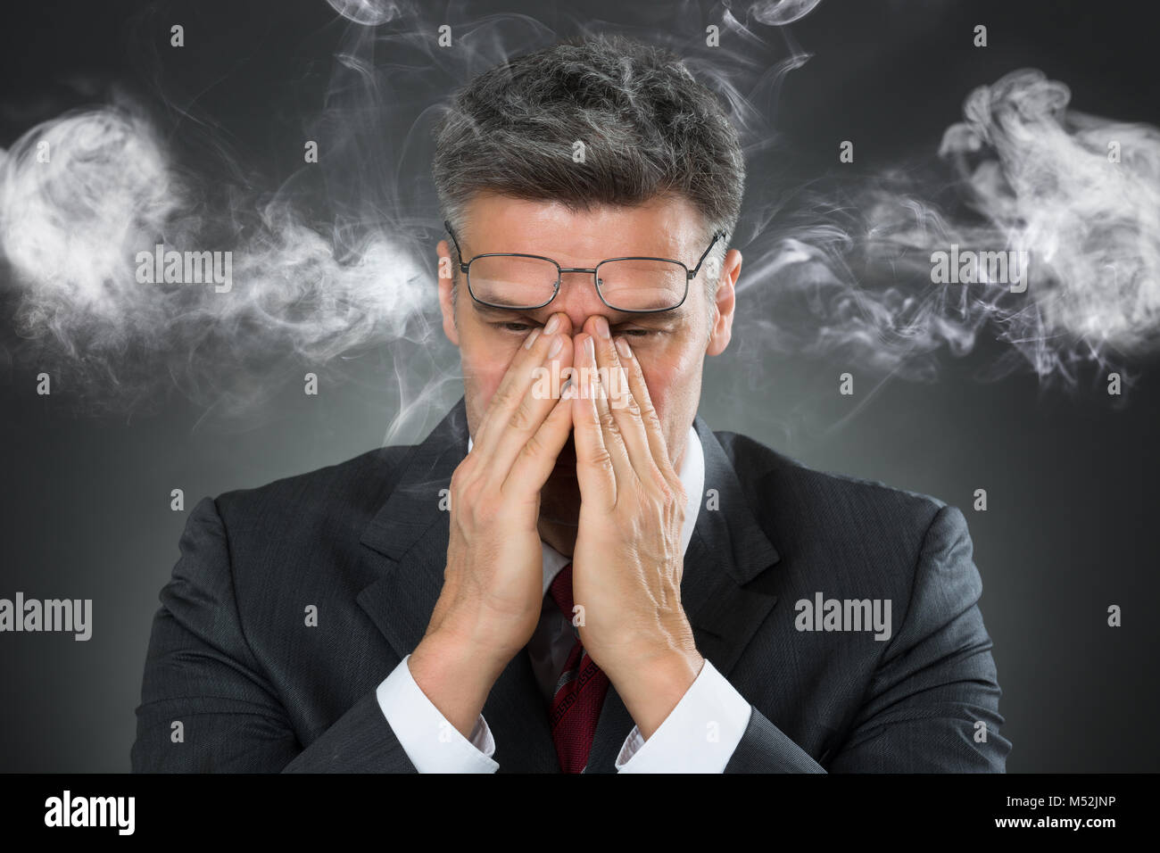 Ritratto di imprenditore che copre la bocca dal fumo su sfondo nero Foto Stock