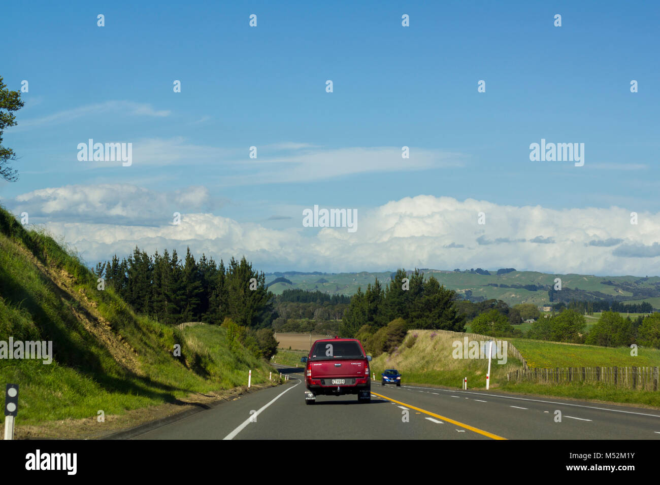 Cars driving su rurale strada asfaltata con vibrante paesaggio verde Foto Stock