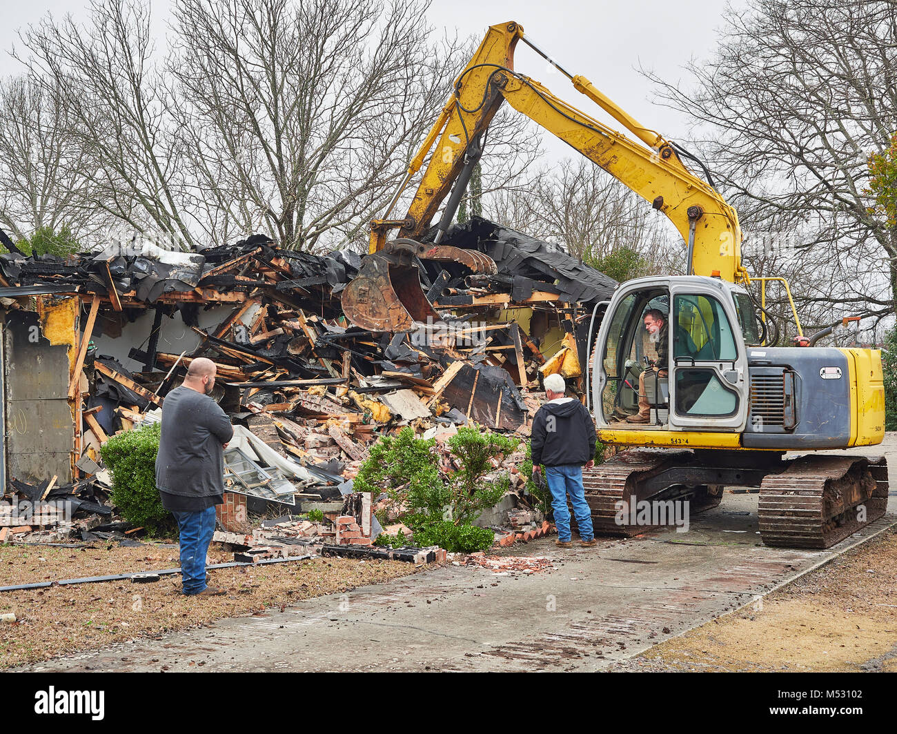 Lavoratori che utilizzano per impieghi pesanti escavatore per aiutare a demolire una casa che ha preso fuoco e bruciati a Montgomery in Alabama, Stati Uniti d'America. Foto Stock