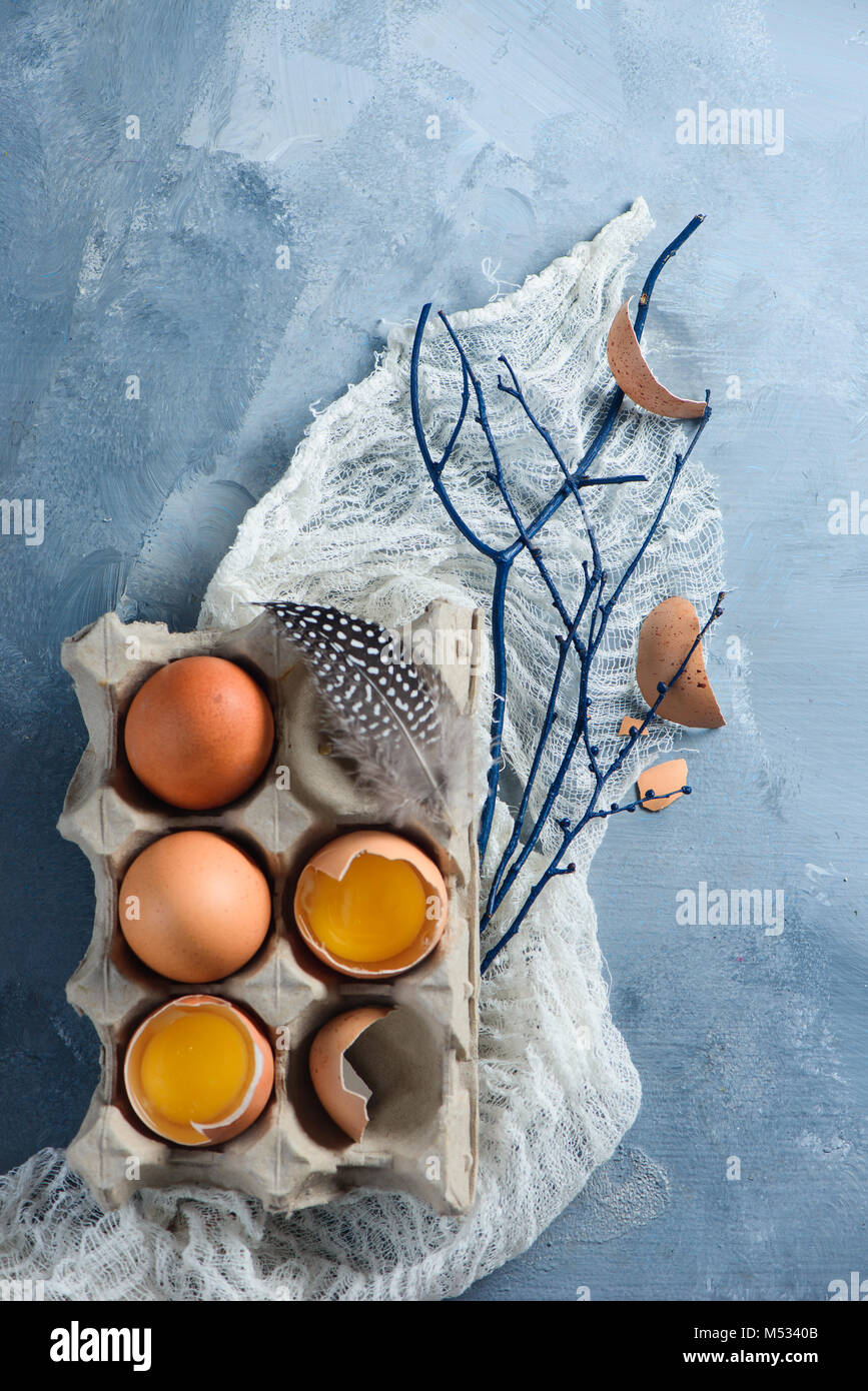 Decorazioni di pasqua concetto con uova fresche in una scatola di cartone, i rami degli alberi e il panno runner su un sfondo di calcestruzzo. Vista da sopra con copia spazio. Foto Stock