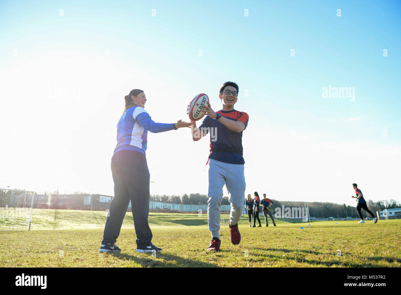 Una scuola PE lezione dove il maestro è di insegnare agli studenti universitari di rugby e gettando e cattura la sfera su una scuola campo sportivo Foto Stock